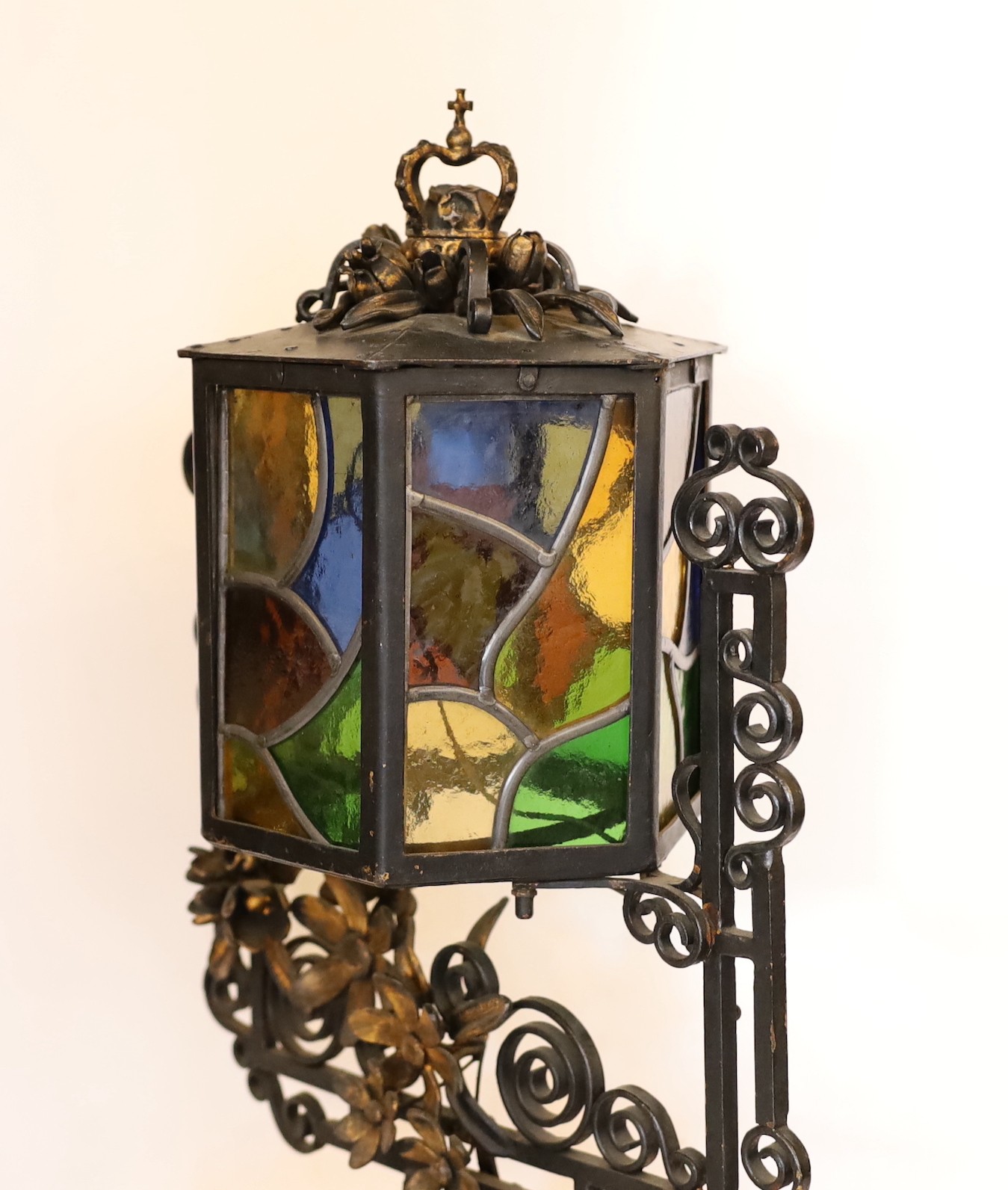 An early 20th century English wrought iron and stained-glass hexagonal lantern style table lamp with crown finial and parcel built black painted finish, height 50cm. width 32cm